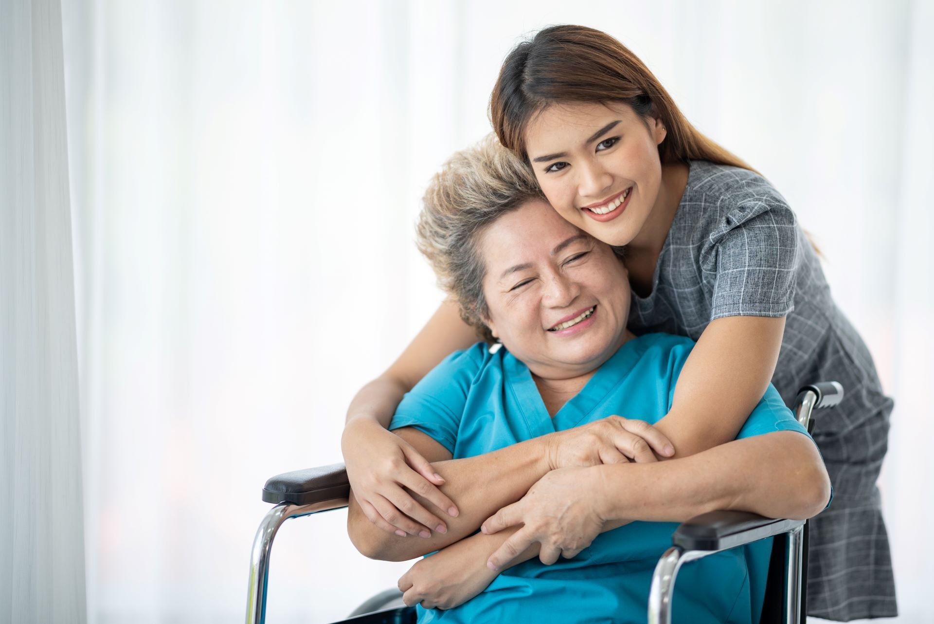 daughter or caregiver giving elderly woman a hug from behind in wheelchair