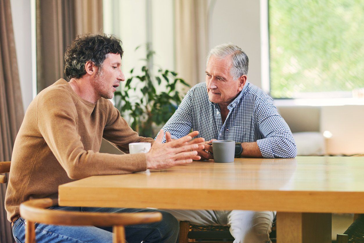 son discussing something with his elderly father at the dinner table