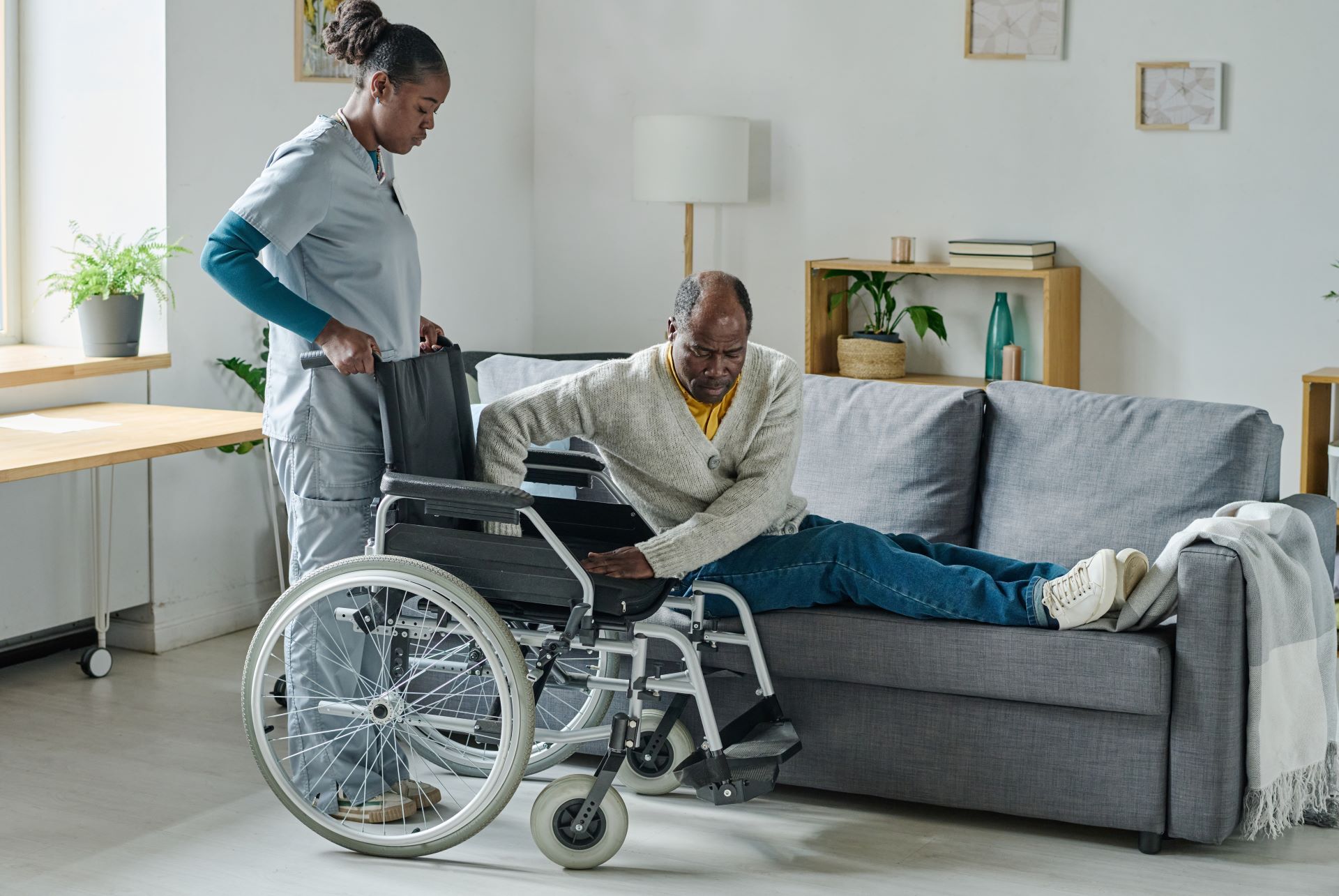 caregiver helping man off couch into wheel chair
