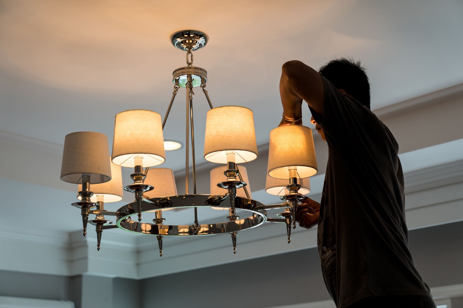 Man on a ladder changing a lightbulb in a chandelier.