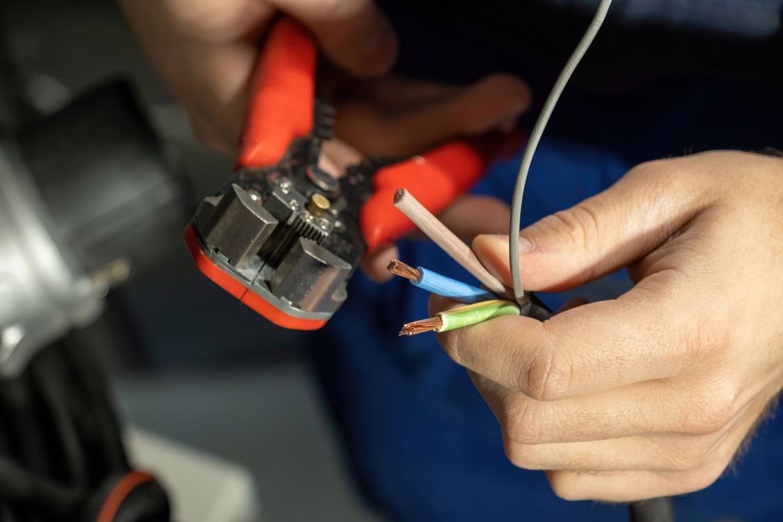 A person stripping electrical wire with red wire strippers.