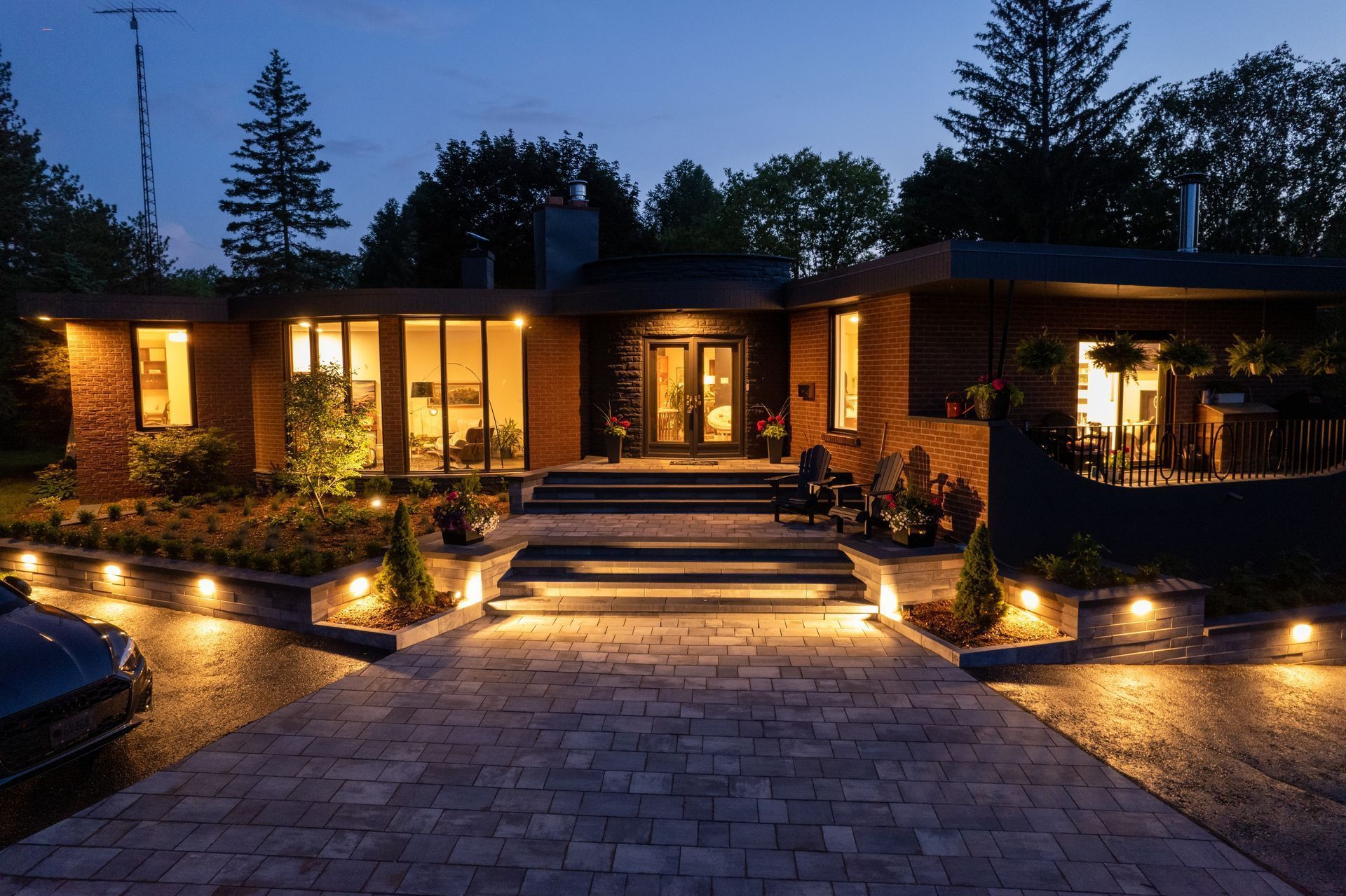 Lit up modern home with a brick driveway and landscaping at dusk.