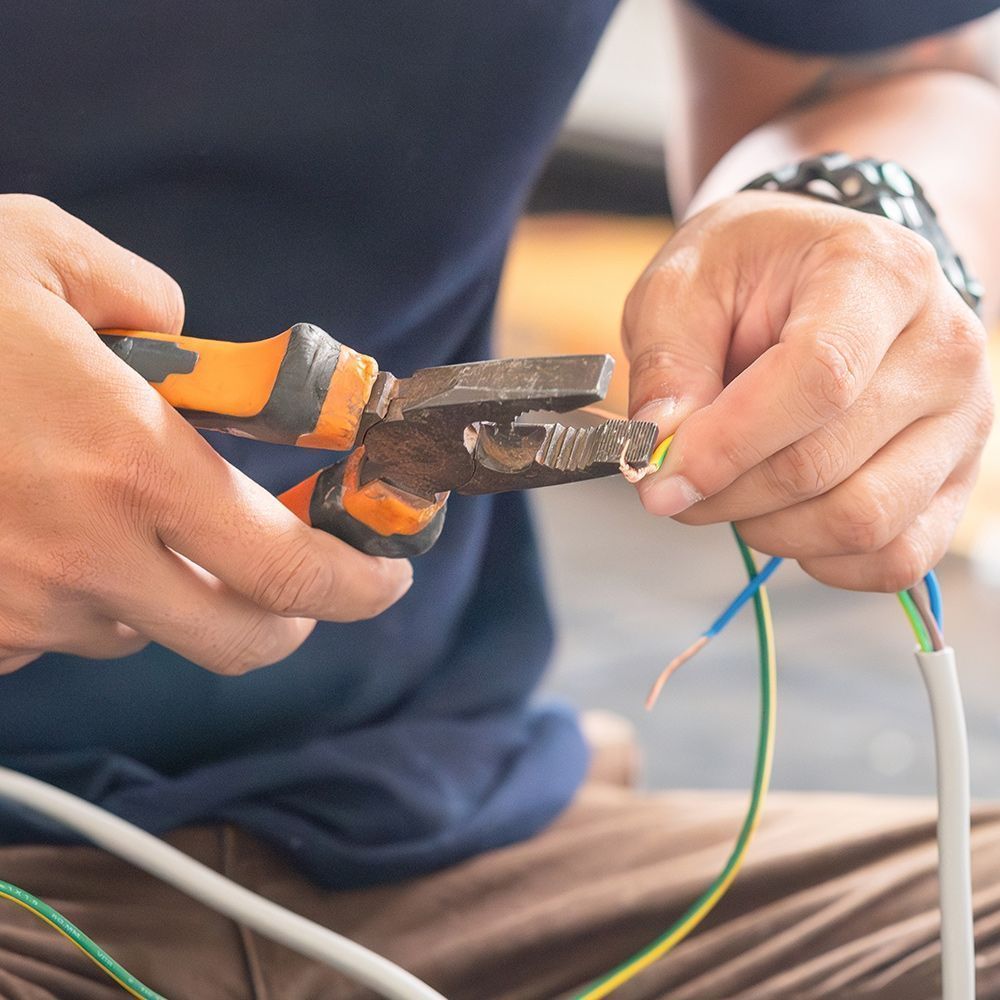 Person using pliers to strip wire, preparing electrical connection.