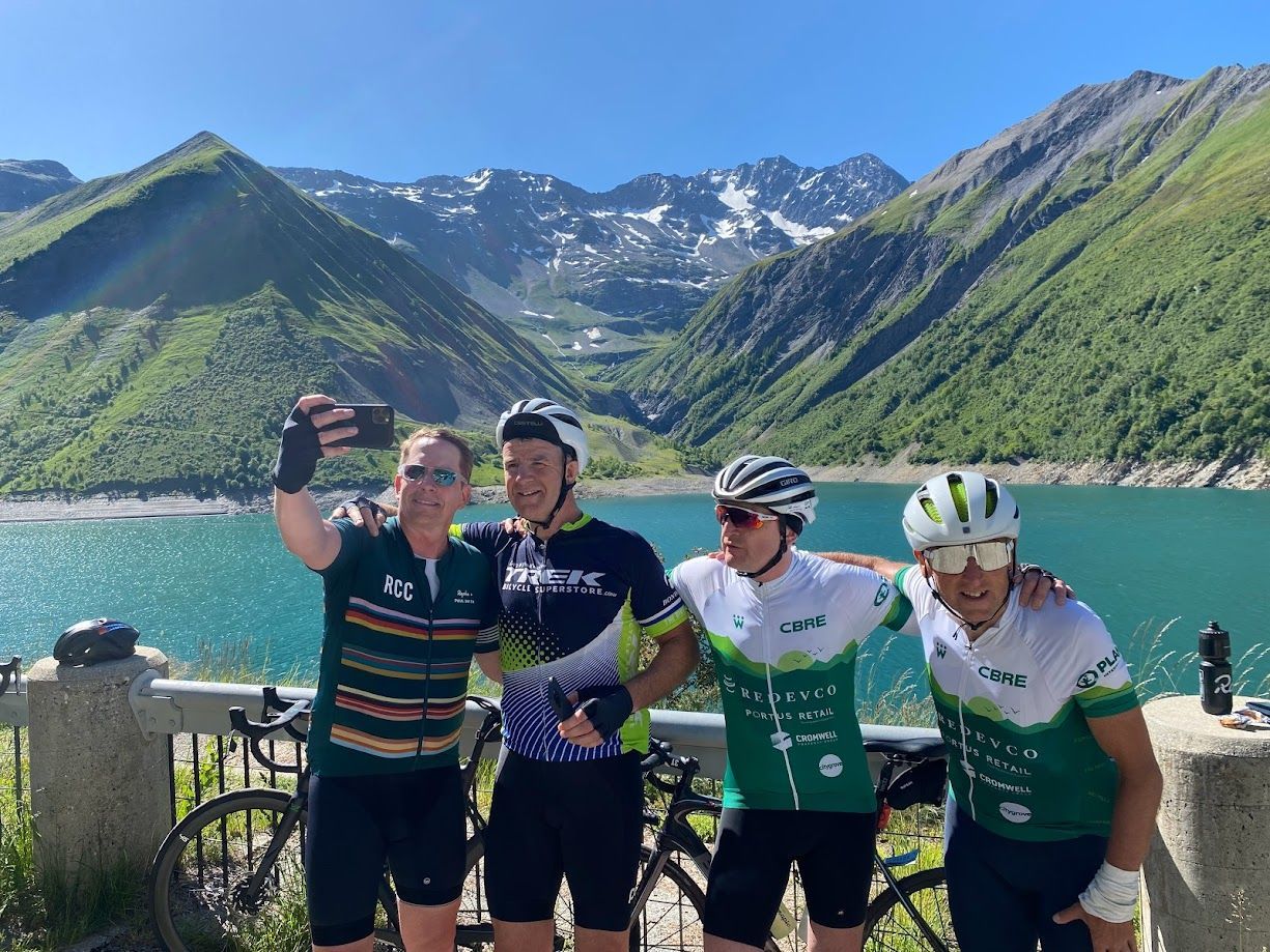 Four cyclists posing by a turquoise lake with mountains in the background