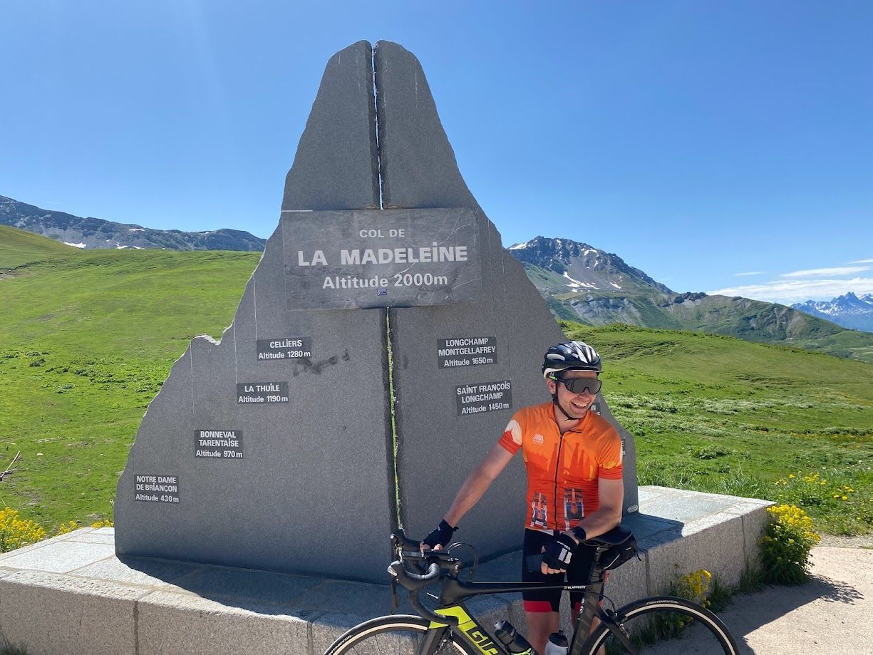 Cyclist beside a large gray memorial stone on a green mountain plateau under a blue sky