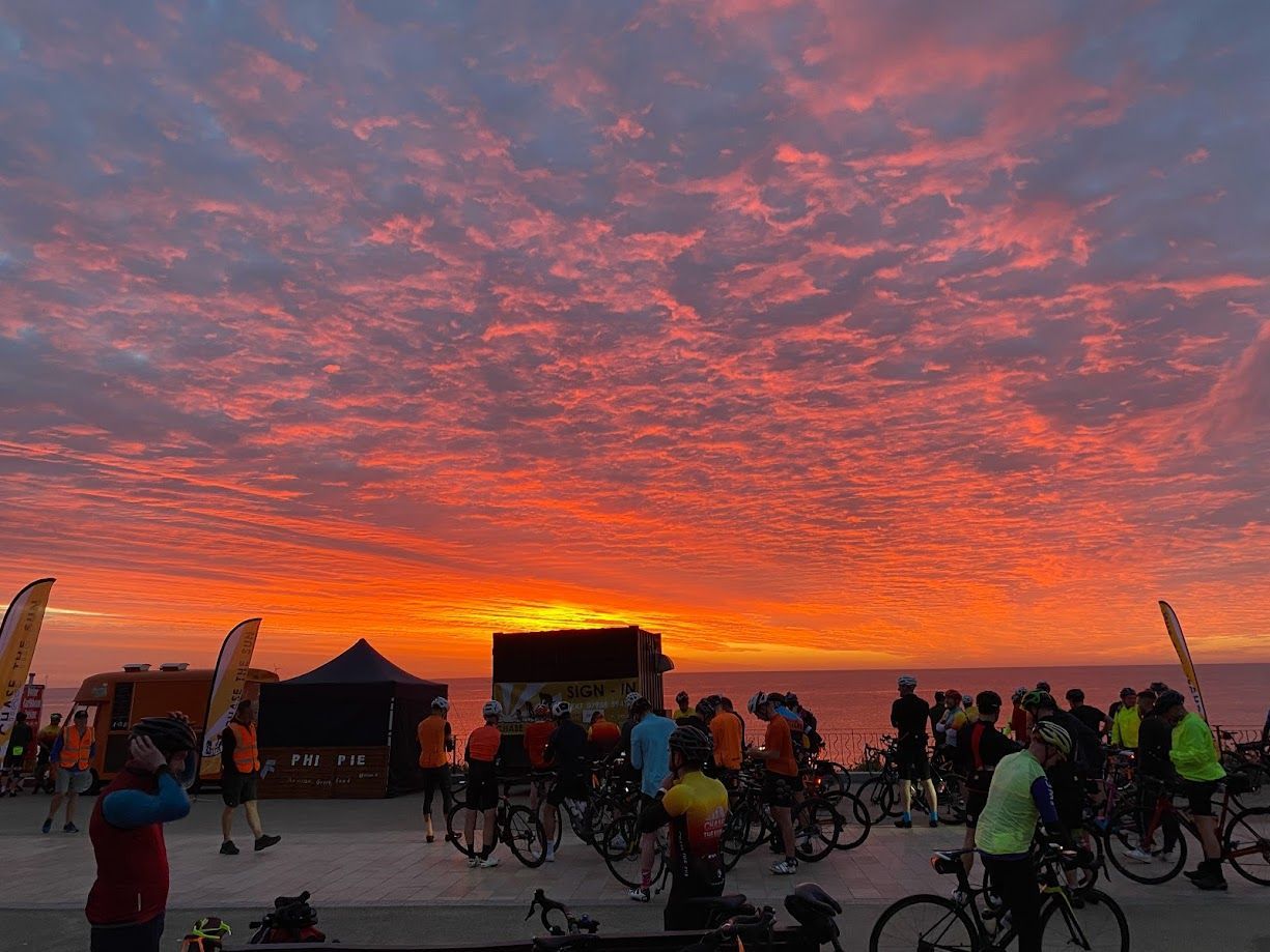 Crowd with bicycles at sunset under a vivid orange and pink sky on the beach