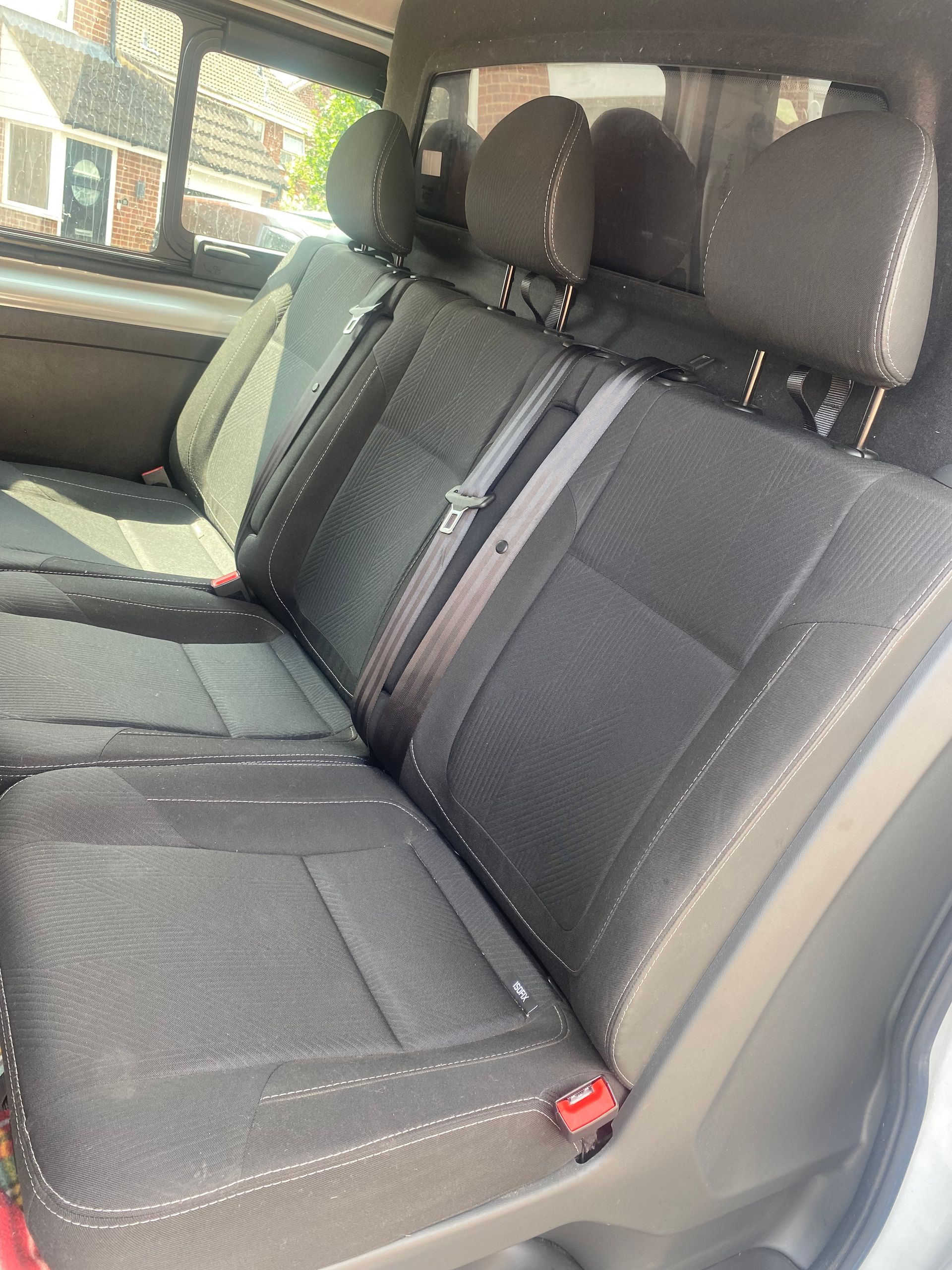 Interior of a vehicle with a black, white, and gray bench seat and a side window showing green fields