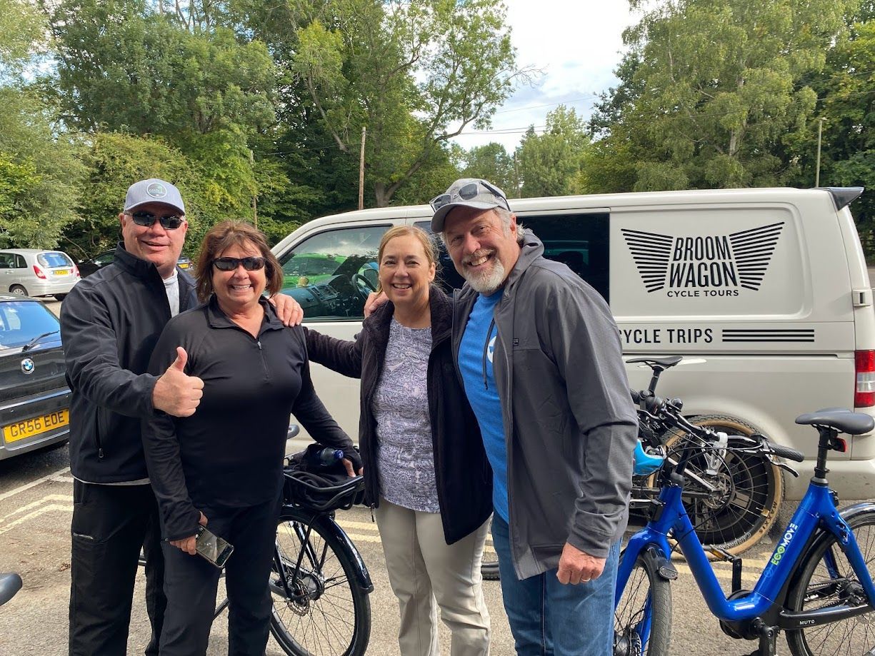 Four people posing with bicycles beside a white van in a leafy outdoor setting.
