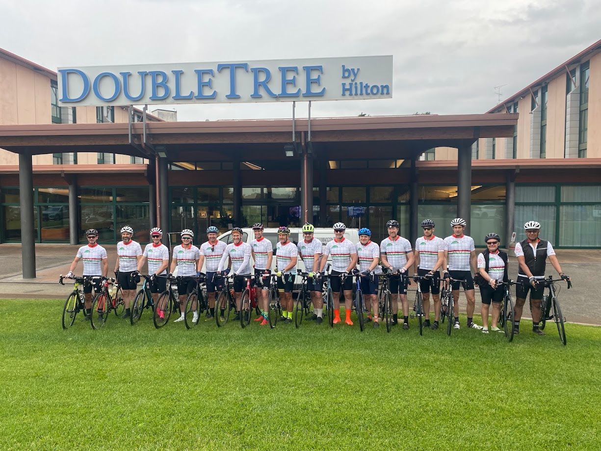 Cyclists posing in front of a DoubleTree hotel, holding bikes on a grassy lawn.