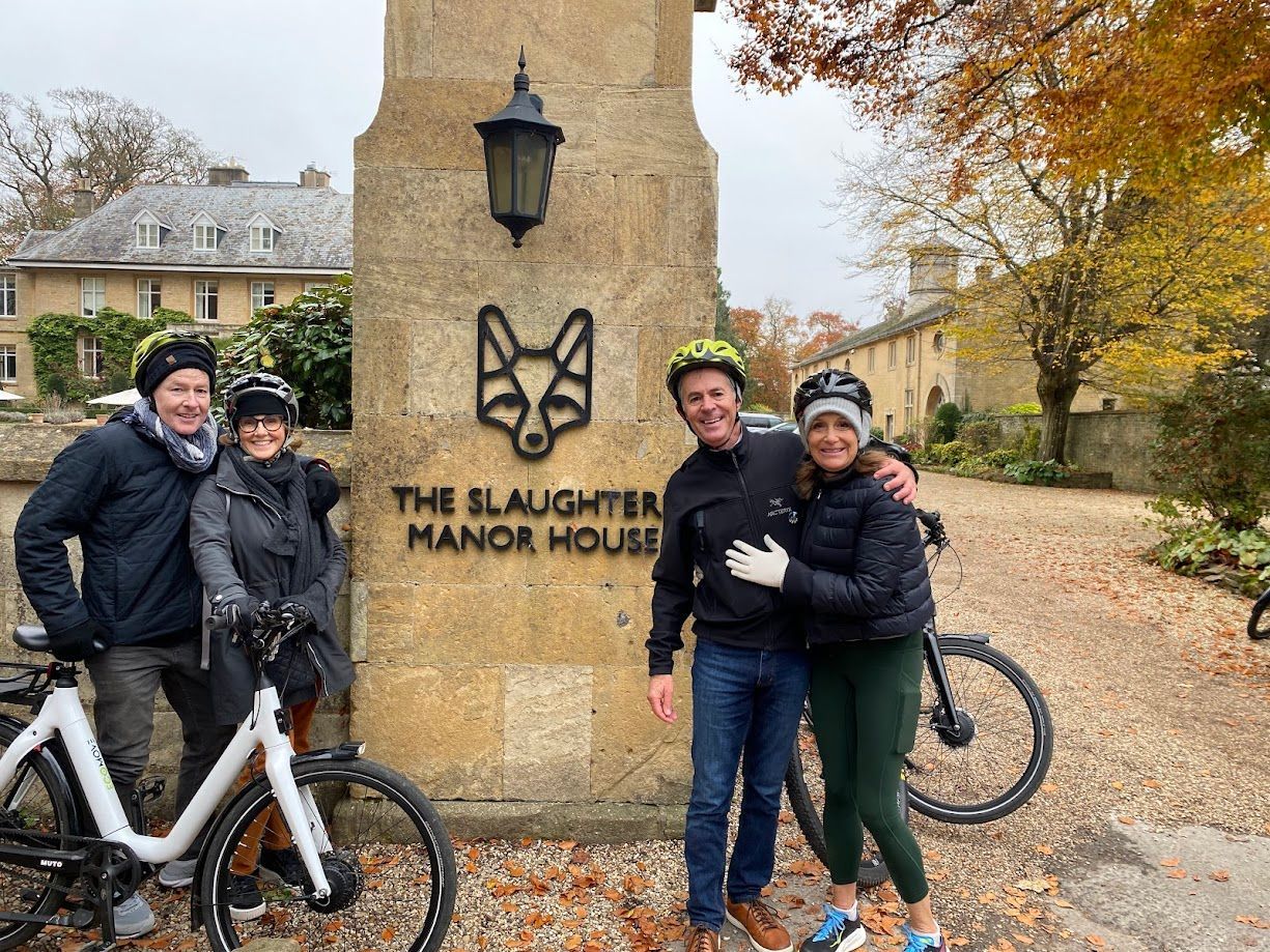 Three cyclists posing by the Slaughter Manor House sign in an autumn setting
