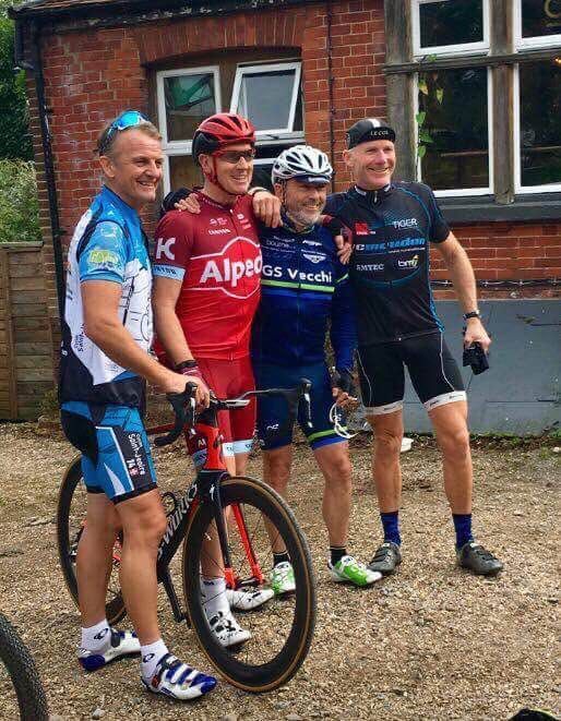 Four cyclists in helmets posing with bikes outside a brick building