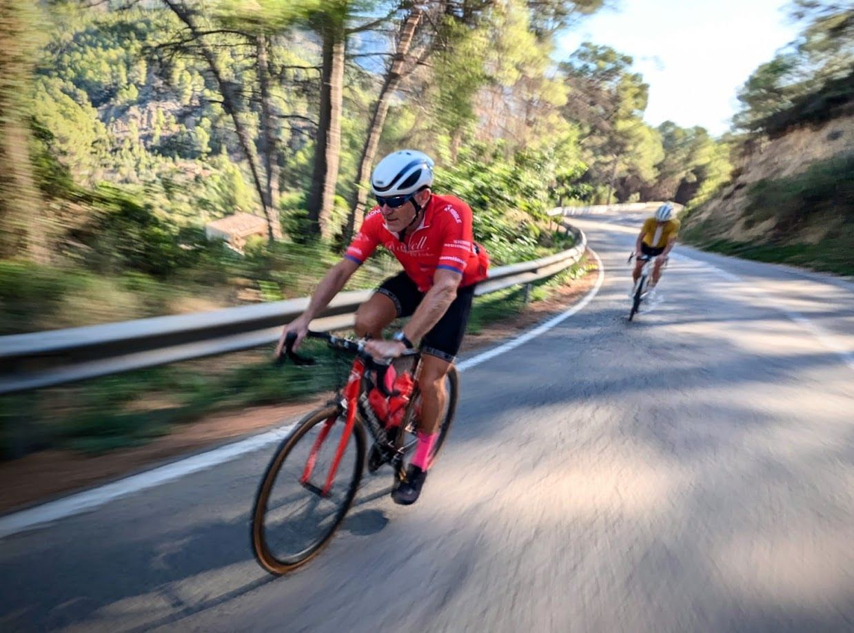 Cyclists in red and yellow gear ride along a winding road through a wooded area