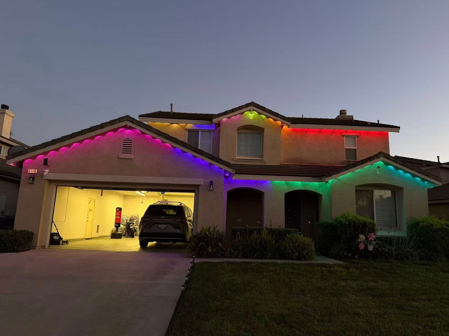 A two-story suburban home at twilight, illuminated by colorful, decorative LED lights along the roofline.