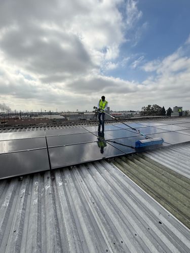 Worker inspecting rooftop solar panels under cloudy sky