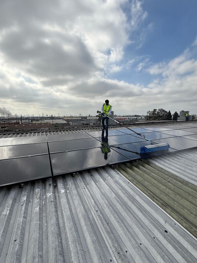 Worker inspecting rooftop solar panels under cloudy sky