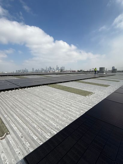 A row of dark solar panels mounted on a slanted residential rooftop, overlooking a neighborhood street with parked cars.