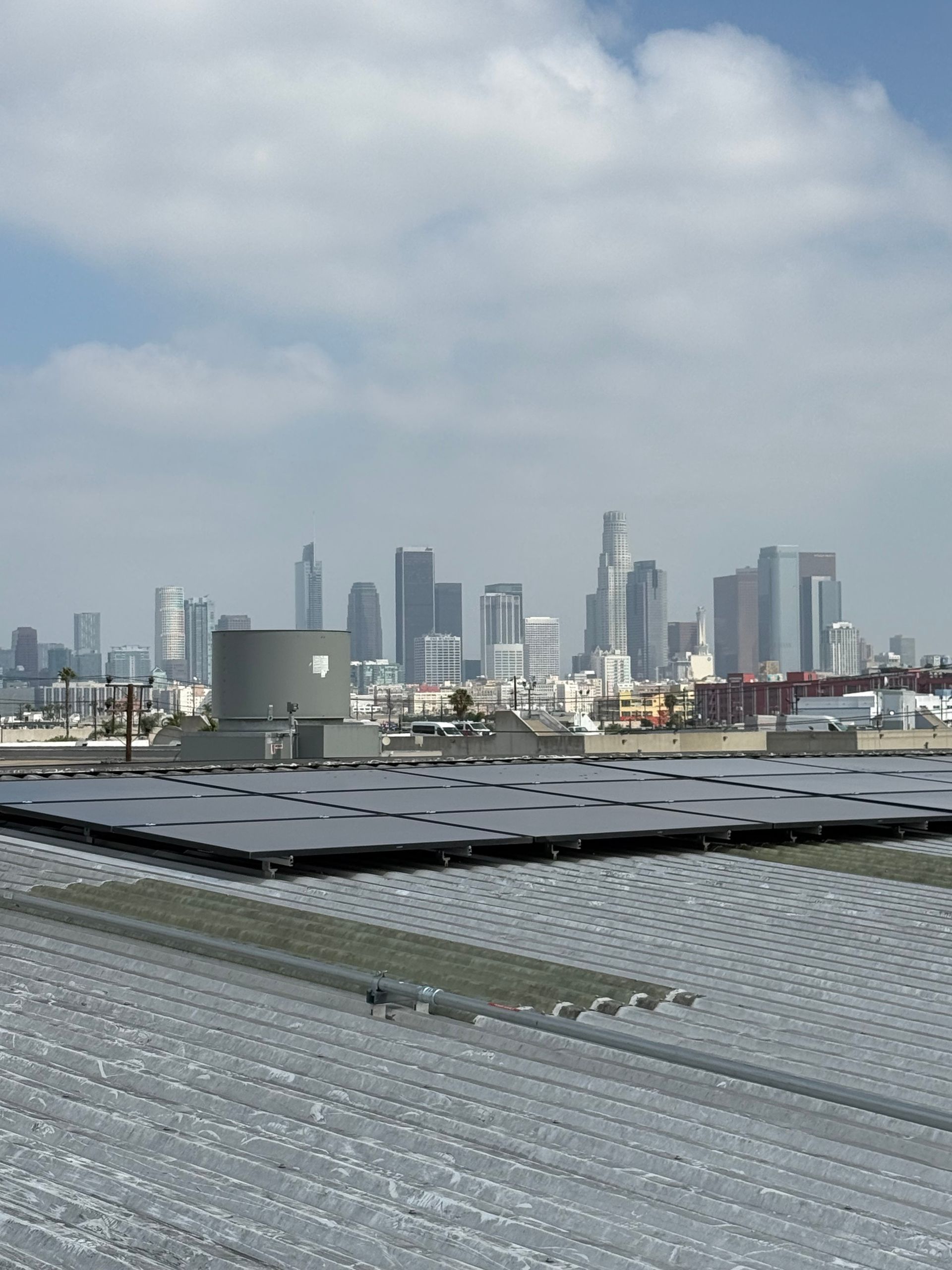 City skyline in the distance beyond industrial rooftops under a cloudy sky.