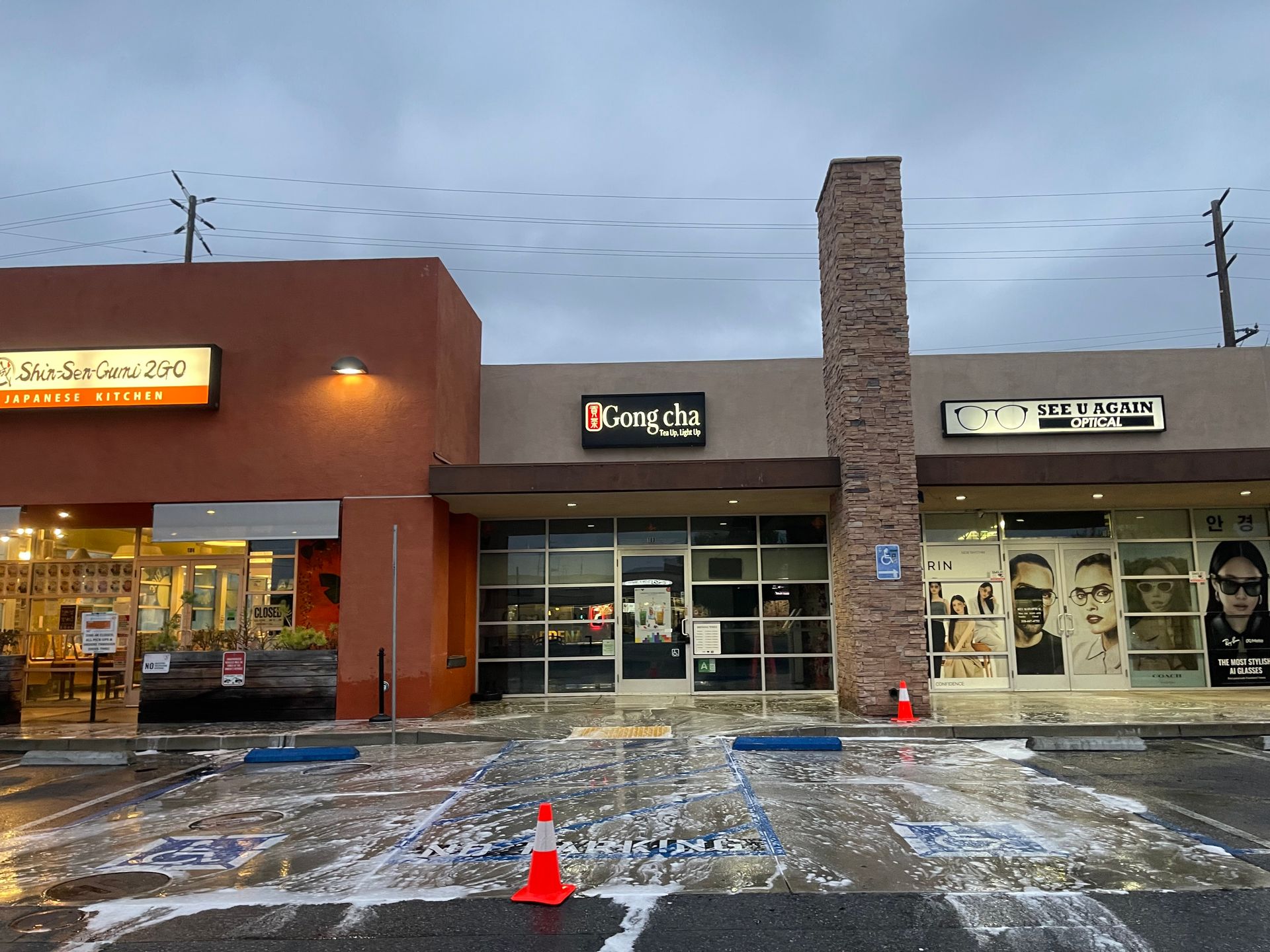 Snowy shopping plaza with storefronts and a stone column at dusk
