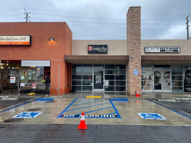Rain-soaked storefronts with accessible parking spaces and a central entrance in a strip mall
