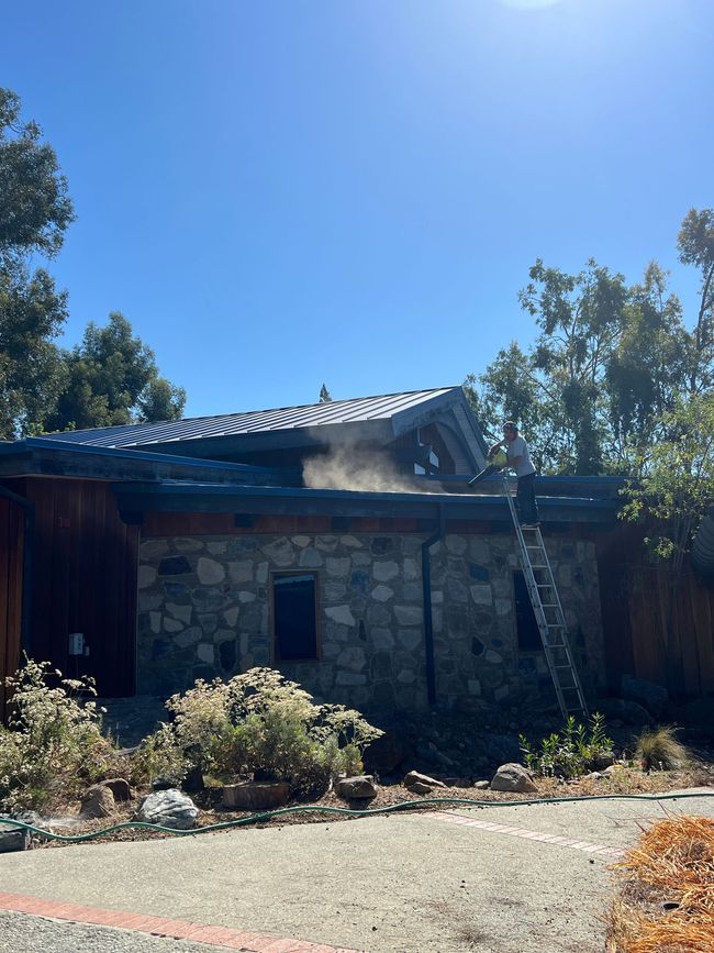 Stone house with blue tile roof among trees under a bright blue sky