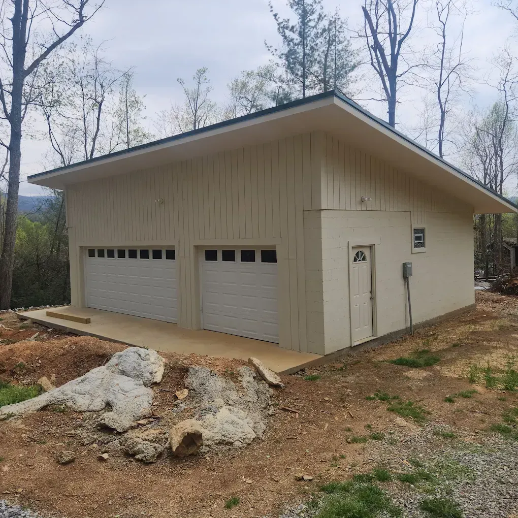 Beige detached garage with two doors, on a wooded construction lot