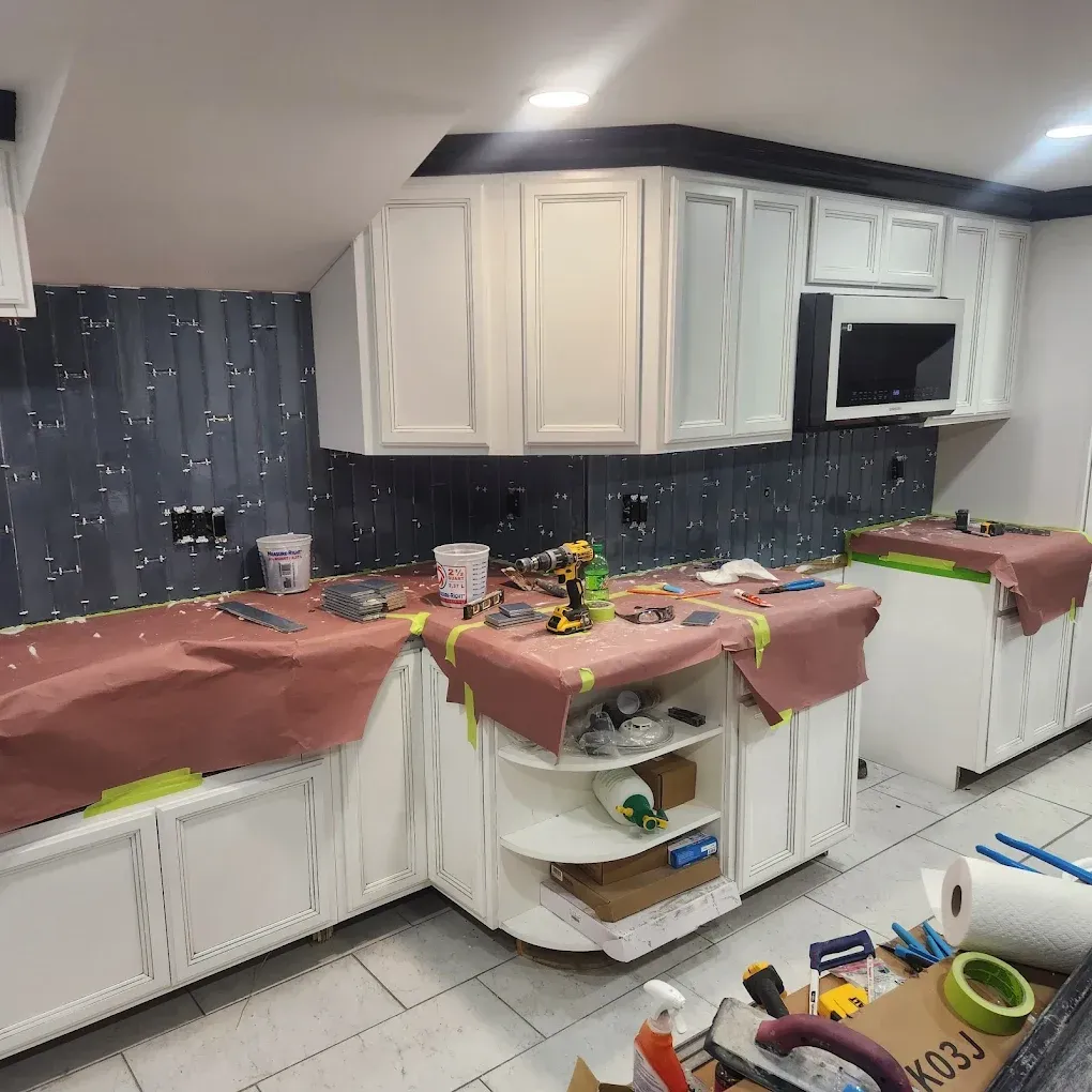 Kitchen cabinets and counters covered with plastic sheeting and tools, suggesting renovation or painting work.