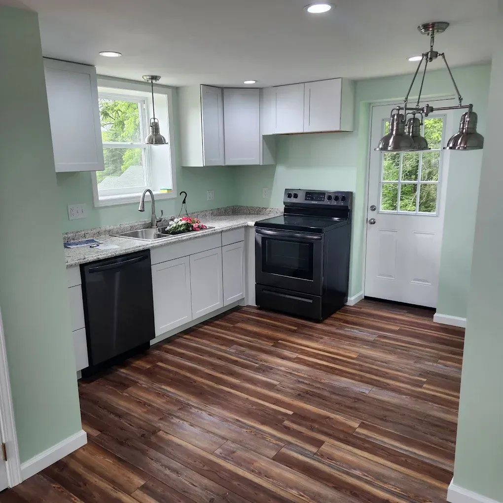 Bright modern kitchen with white cabinets, black appliances, and wood-look flooring