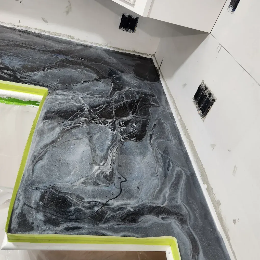Black-and-gray swirled flooring being installed in a room with white walls and cabinets