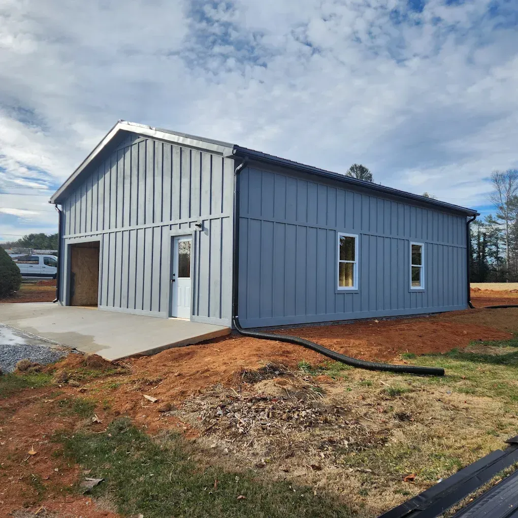 Blue metal barn-style building with white trim, garage door, and gravel lot under a cloudy sky