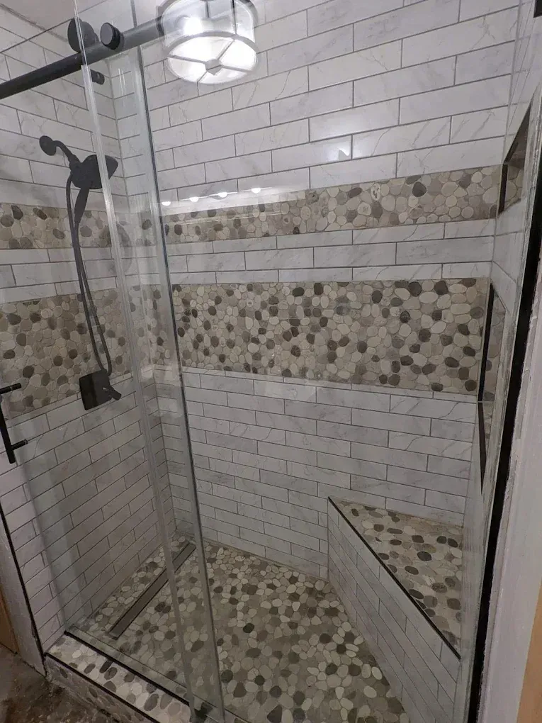 Tiled shower with glass door, wall-mounted showerhead, and pebble accent trim.