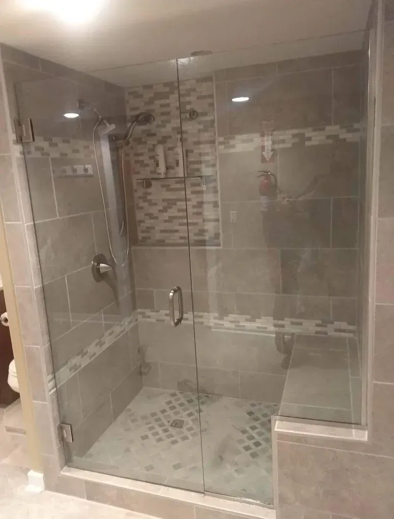 Glass-enclosed tiled shower with mosaic accent strip and built-in bench.