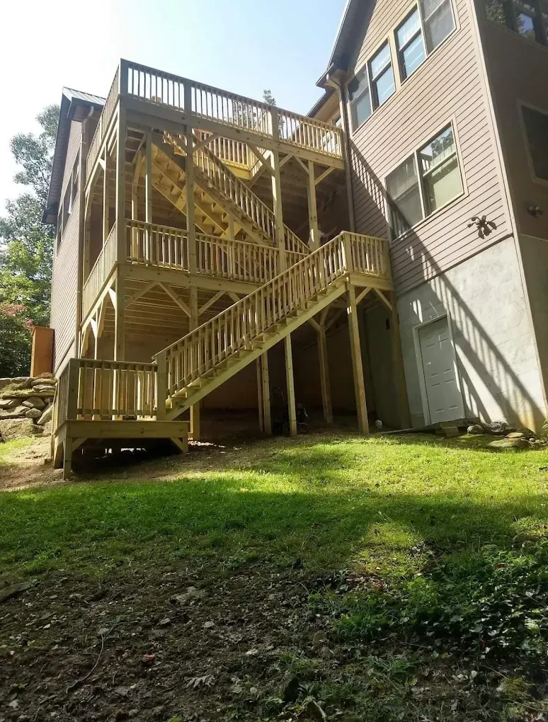 Wooden outdoor apartment staircase and deck beside a beige building, overlooking a grassy yard.