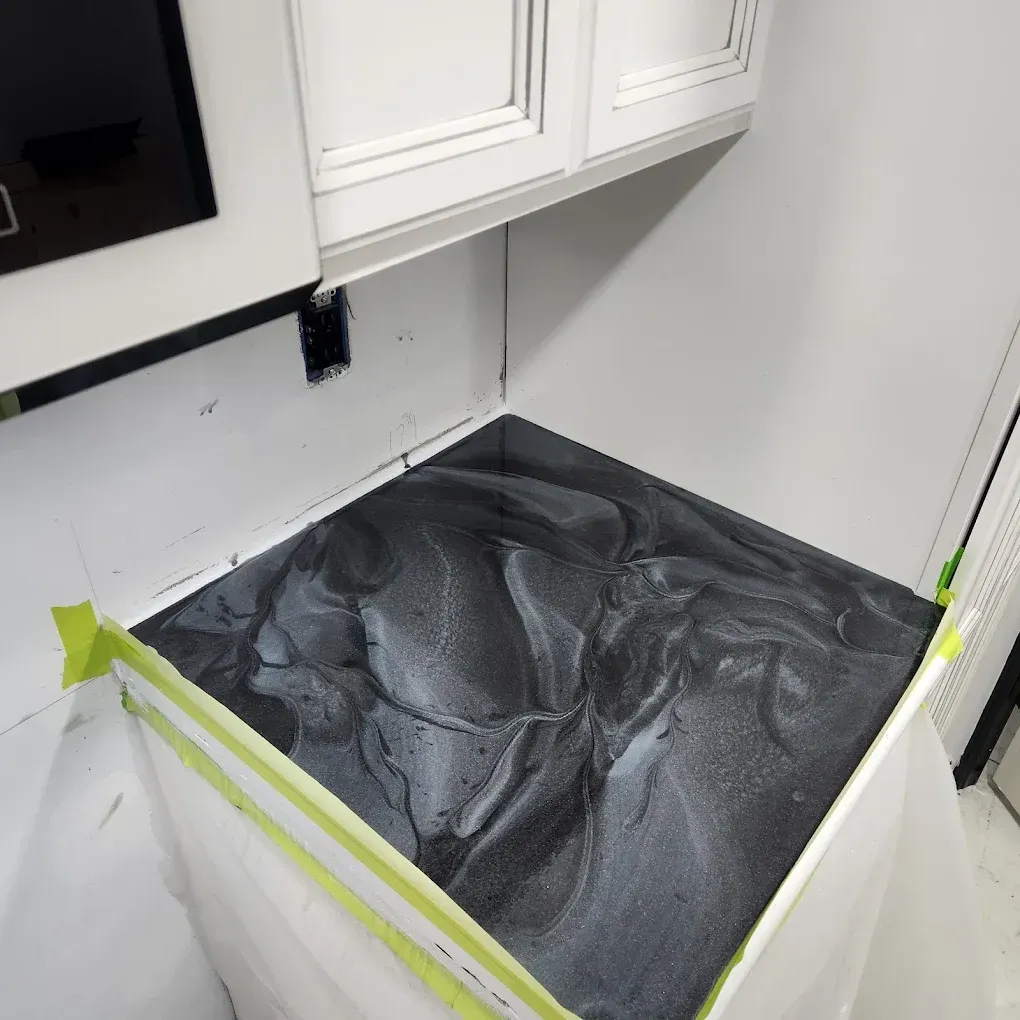 Kitchen countertop covered with black speckled material, masked with tape and plastic sheeting