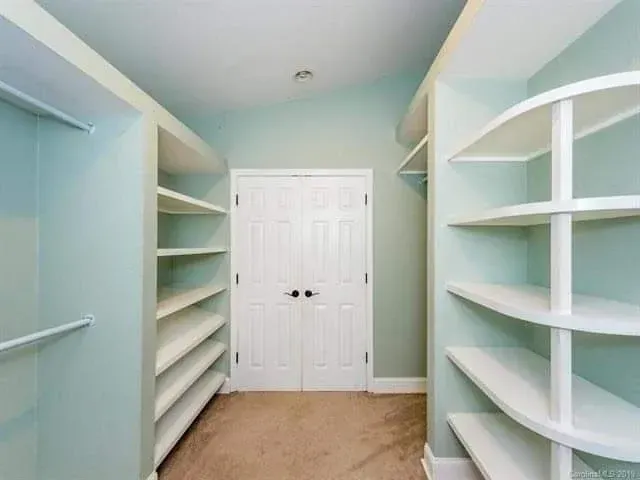 Bright walk-in closet with white built-in shelves, light blue walls, and closed double doors at the back