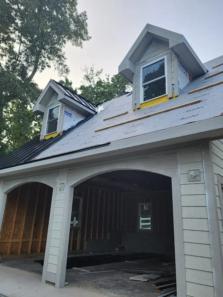 Gray garage with two dormer windows and open bays under construction, with debris on the floor.