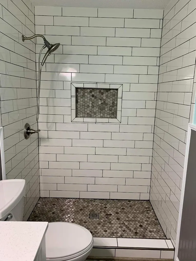 Small tiled shower with a rainfall head, mosaic accent wall, and a toilet visible at left.
