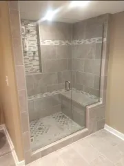 Walk-in tiled shower with glass door and bench seat in a beige bathroom