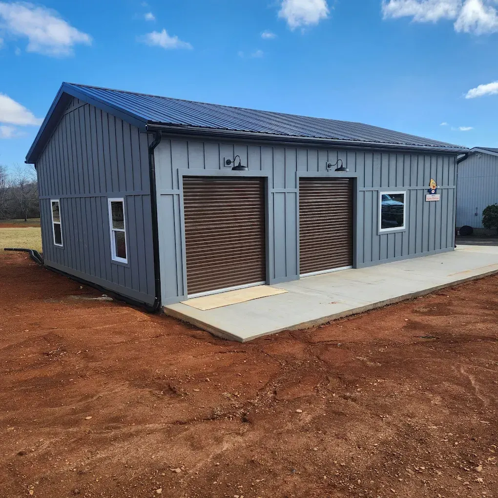 Gray metal garage building with two brown roll-up doors on a concrete slab in a dirt lot under a blue sky