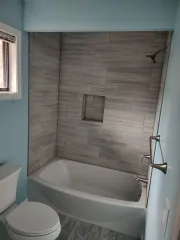 Small bathroom with a white tub-shower, gray tile wall, toilet, and blue walls.