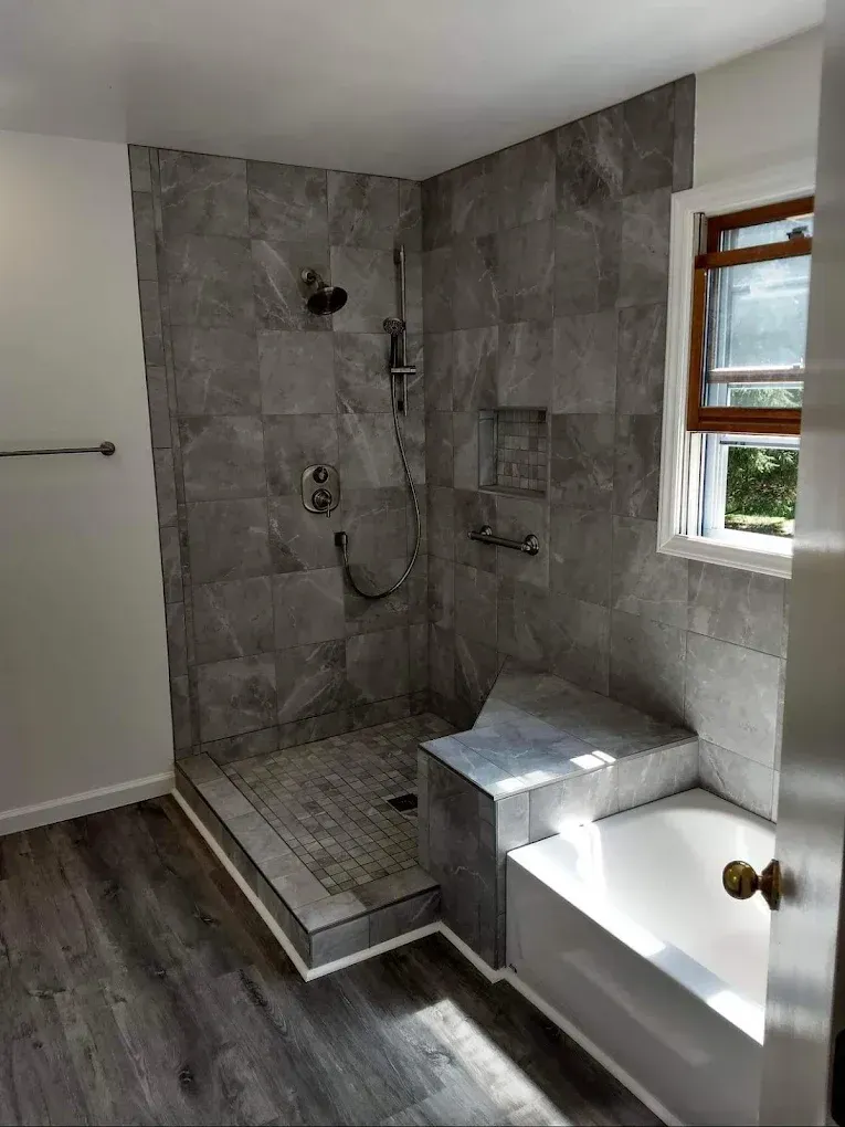 Gray tiled walk-in shower beside a bathtub in a modern bathroom with a window.