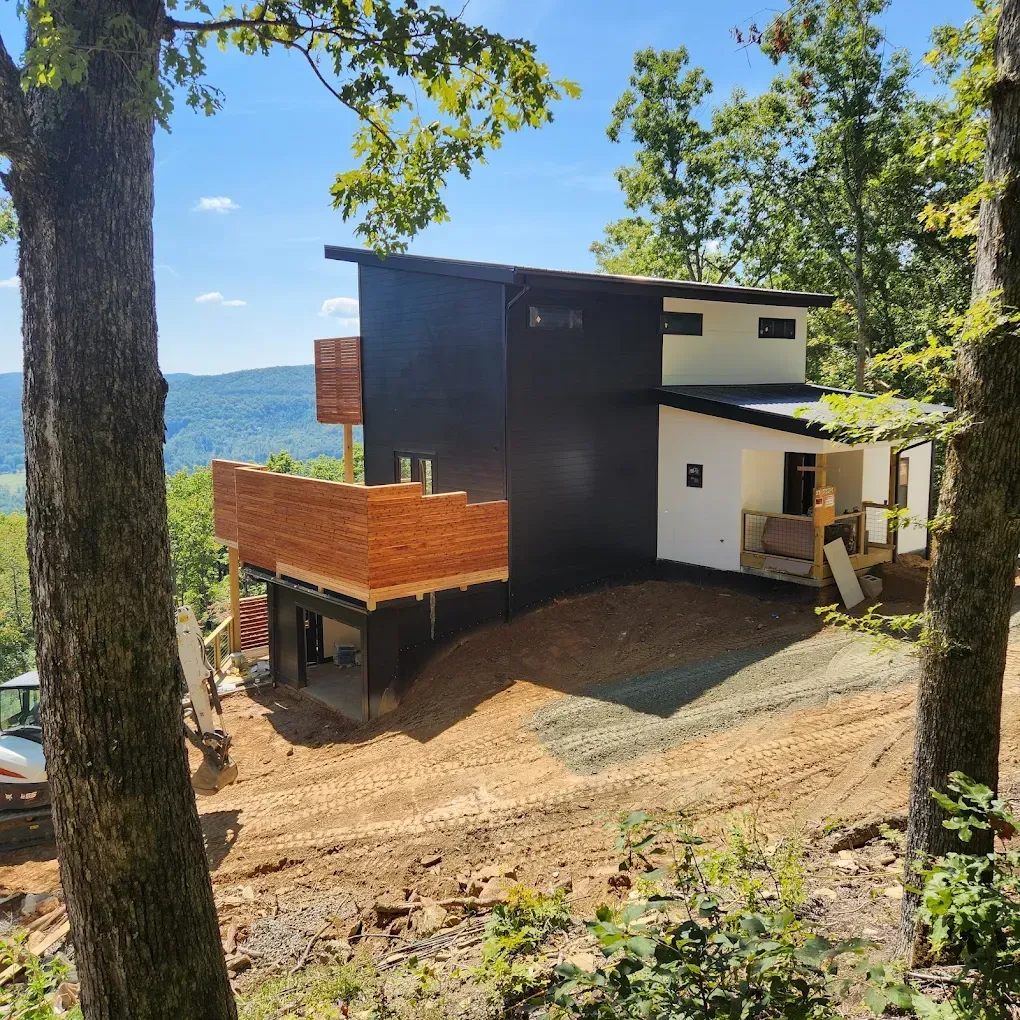 Modern house with black and white exterior on a wooded hillside overlooking water