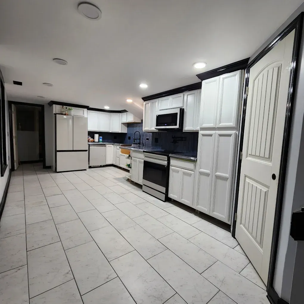 Modern white kitchen with black accents, tile floor, stainless appliances, and recessed ceiling lights
