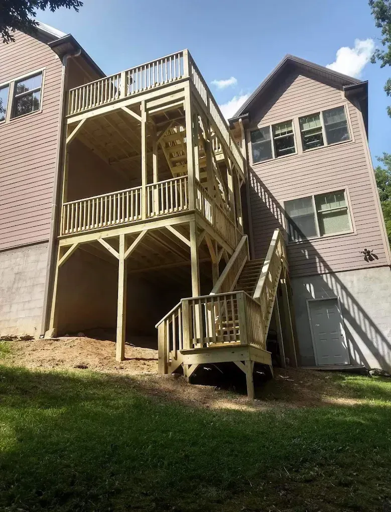 Multi-level apartment building with beige siding and wooden staircases, viewed from a grassy slope