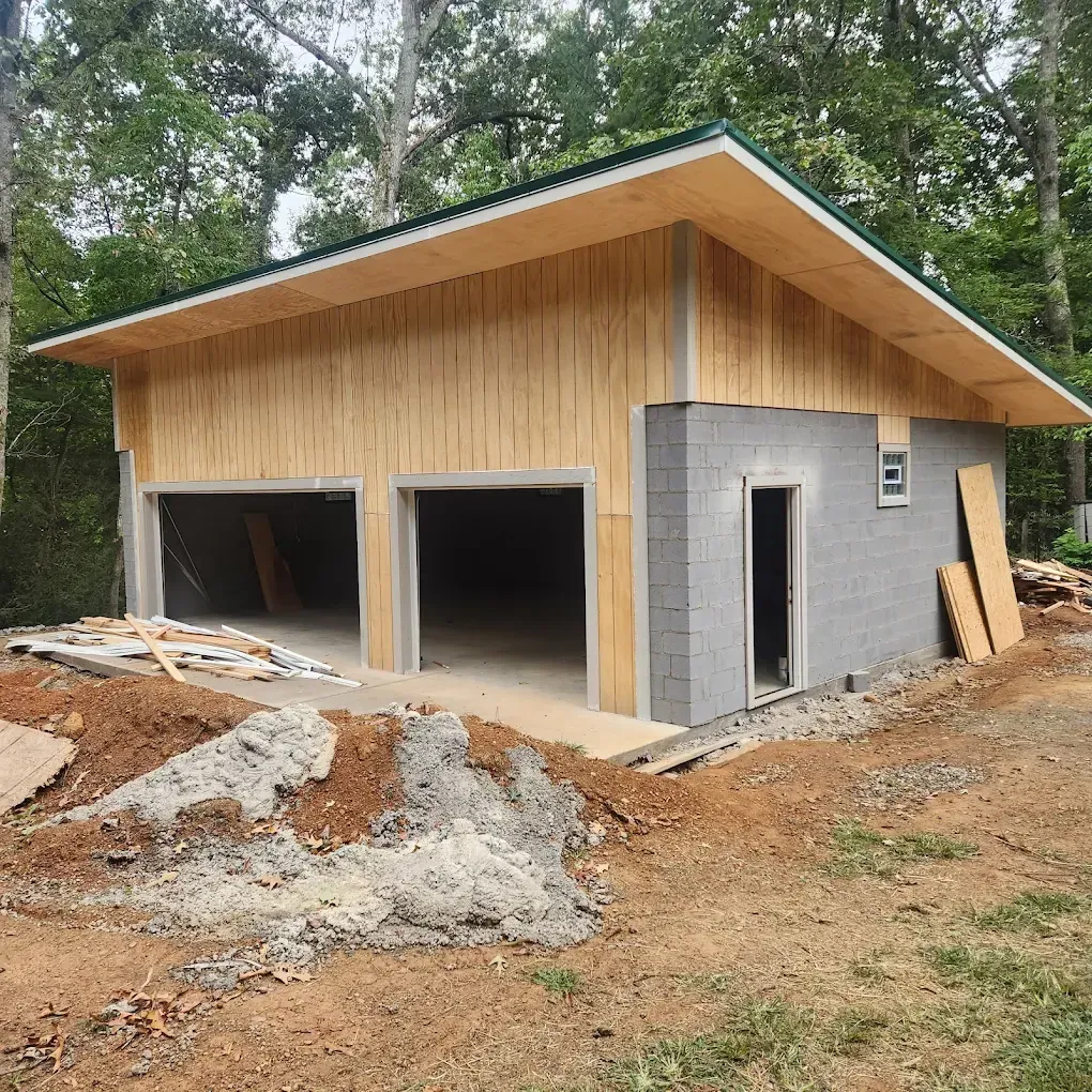 Partially built modern garage with wood siding, concrete front, and open bays in a wooded lot