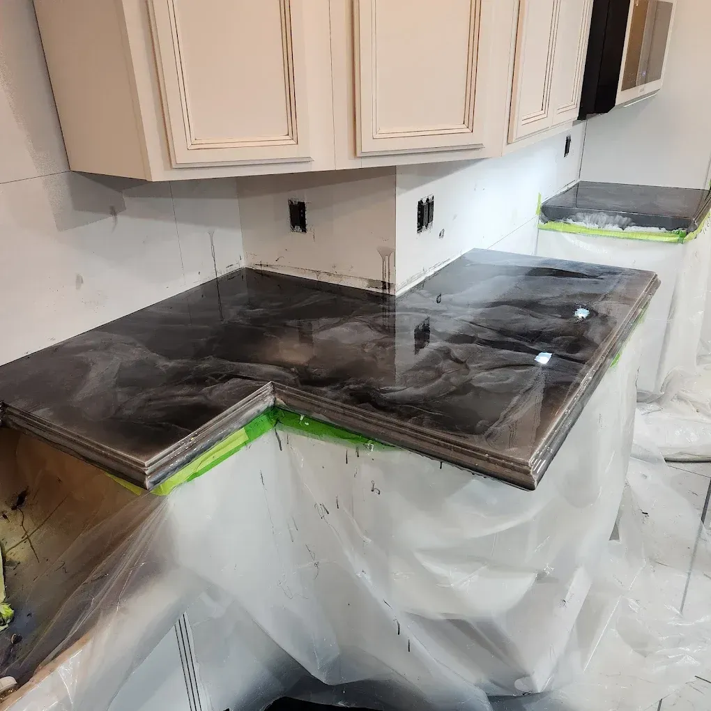 Kitchen countertop and upper cabinets wrapped in plastic during renovation, with dark stone slabs installed.