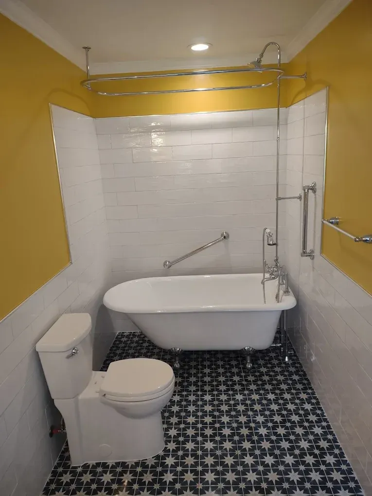 Small bathroom with clawfoot tub, toilet, yellow walls, white tile, and patterned black-and-white floor.