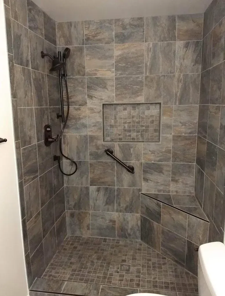Tiled walk-in shower with bench, wall niche, handheld showerhead, and mosaic floor.