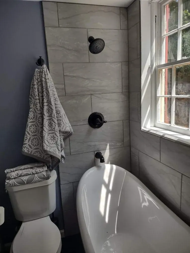 Modern bathroom with a freestanding tub, tiled shower wall, towel, toilet, and window light