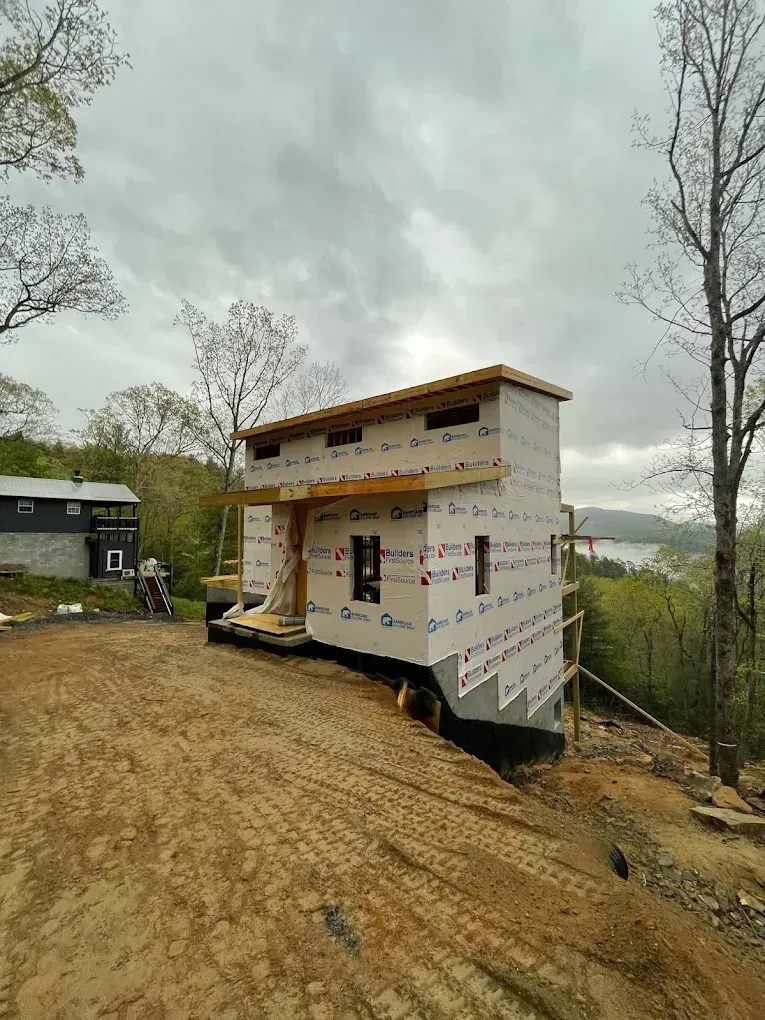 Partially built white house on a dirt slope under cloudy sky, with mountains in the distance