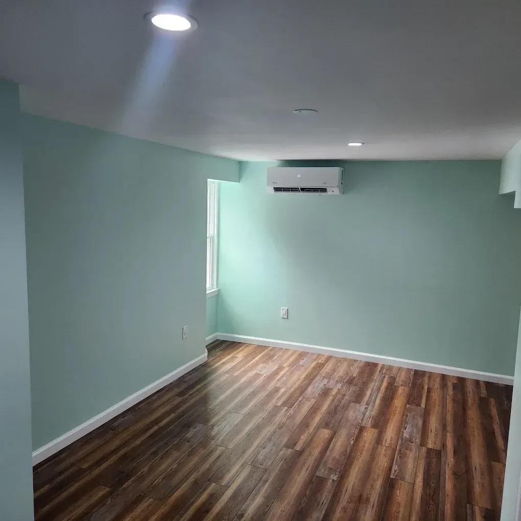 Empty room with mint green walls, wood floors, recessed ceiling lights, and a wall-mounted air conditioner.